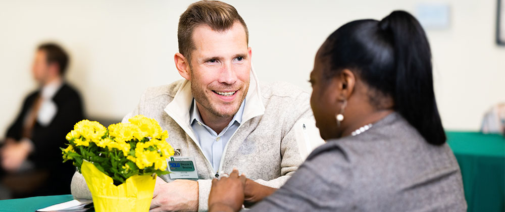 Two students sitting at a table talking and smiling at each other